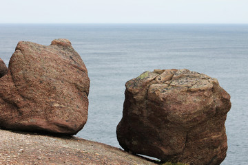 Two large boulders resting on the edge of the cliff, Signal Hill, Newfoundland. Background of blue water and blue sky.