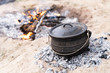 cast iron pot being used to cook a camping meal with coals and a wood burning camp fire
