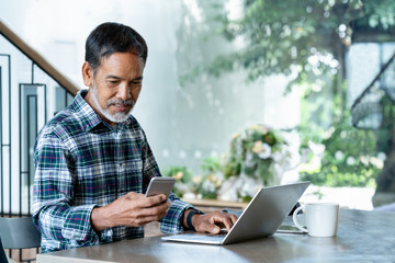 Smiling attractive mature man with white, grey stylish short beard using smartphone gadget serving internet in modern office,co-working space,coffee shop cafe. Old man using social network technology.