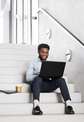 Wall Mural - business, people and technology concept - african american businessman with laptop working computer at office stairs