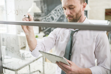 Wall Mural - Waist up portrait of handsome businessman wearing shirt and tie brainstorming problem and writing on glass wall in modern office, copy space