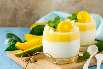 Mango panna cotta with fresh mango and topping with mango jelly on a stone or slate background. Traditional italian dessert. Copy space.