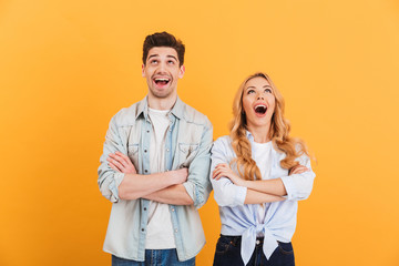 Image of excited people man and woman in basic clothing posing with arms crossed and looking upward, isolated over yellow background