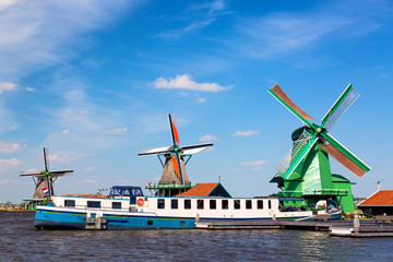 Wall Mural - Dutch typical landscape. Traditional old dutch windmills with cruise ship and blue sky in the Zaanse Schans village, Netherlands. Famous tourism place.