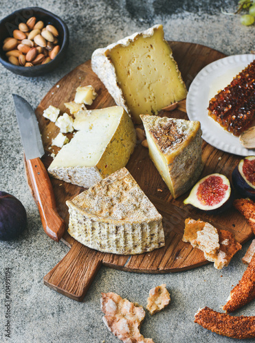 Cheese platter with cheese assortment, figs, honey, fresh bread and nuts on board over grey concrete background Canvas Print