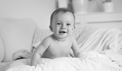 Wall Mural - Black and white portrait of smiling baby boy lying on big soft pillow