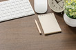 Mockup of white keyboard, mouse, blank notebook, pencil,alarm clock and houseplant on wooden table