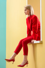 Side View Of Beautiful Blond Woman In Stylish Red Suit And Shoes Sitting On Decorative Window