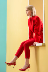 side view of beautiful blond woman in stylish red suit and shoes sitting on decorative window