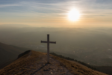 Cross on top of Mt. Serrasanta (Umbria, Italy), with warm golden hour colors and sun low on the horizon