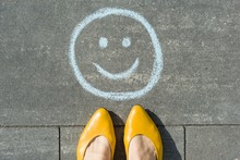 Symbol Of Happy Smiley Drawn On The Asphalt And Woman Feet