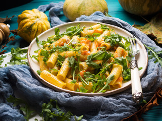 Pasta with baked pumpkin, arugula and onion. Rustic green autumn background with pumpkins and dry leaves. Fall food still life flat lay