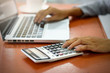 © Chayanin Wongpracha - The hand of Beautiful businesswoman uses a calculator in the office. With laptop computer on the wood table. Business and Technology Concepts.