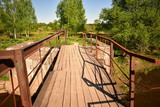 Fototapeta Tulipany - landscape wooden bridge over the river, rusty metal railings, background green trees, blue sky