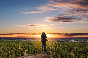 Wall Mural - a man with backpack standing on the mountain enjoying beautiful sunrise, and pine forests
