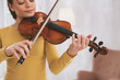 Relaxed atmosphere. Concentrated young female looking at strings while playing the violin