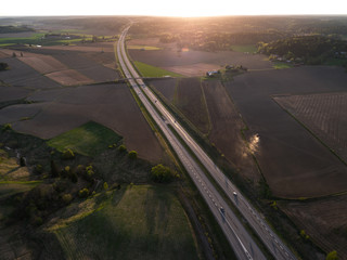 Aerial view of highway leading towards setting sun with cars on the highway and tractor on the field