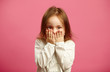 © Ilshat - Little girl covered her mouth with hands on pink isolated background.
