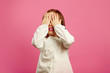 © Ilshat - Little girl covered her eyes with hands and smiles on pink isolated background.