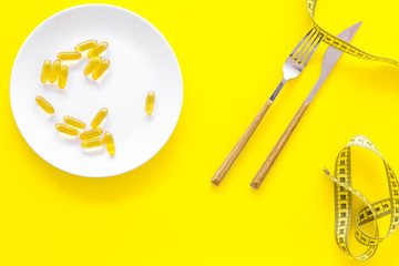 Dietary supplement for well-being. Fish oil or omega-3 capsules on plate near measuring tape on yellow background top view copy space