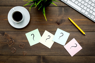 Poster - Question mark on sticky notes on office desk on dark wooden background top view. FAQ concept. Working with clients. Troubles in work.
