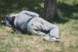 © Srdjan - Old barefoot homeless or refugee man sleeping on the grass in the park using his travel bag as pillow, social documentary street concept