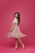 © oes - Young stylish girl in pink light skirt and white T-shirt on pink isolated background with place for text. The girl cheerfully dances and jumps like a ballerina