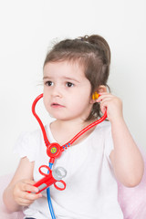 Wall Mural - Cute little girl with stethoscope playing on sofa at home with mother arms