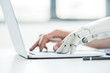 selective focus of human and robot hands typing on laptop at workplace