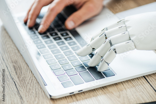 Fotografía close-up view of human and robot hands typing on laptop at workplace