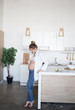 © Svetlana - A pregnant woman is standing in the kitchen in jeans and a white shirt. Pregnant woman looking at stomach