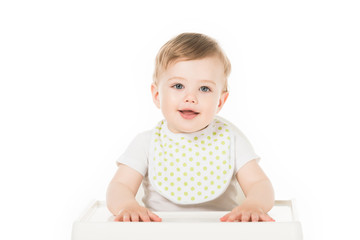 smiling baby boy in bib sitting in highchair isolated on white background