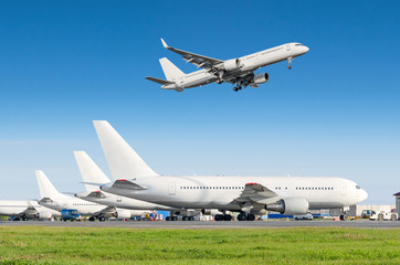 Wall Mural - Passenger aircraft row, airplane parked on service before departure at the airport, other plane push back tow. Airplane landing to the runway in the blue sky.