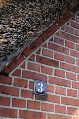 Traditional frisian brick house with a thatched roof and a blue iron house number plate