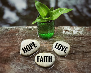 Wall Mural - Religion and belief concept - ‘Hope, faith and love’ words on white pebbles. With blurred vintage styled background.