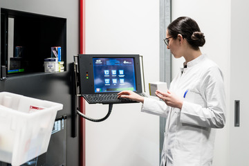 Low-angle rear view of an experienced female pharmacist using a computer while managing the drug stock in a contemporary pharmacy with modern technology