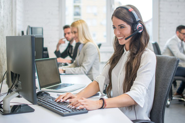 Wall Mural - Attractive young woman working at call center office with her colleagues.