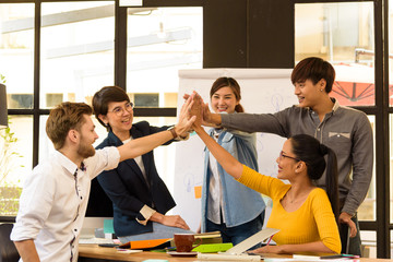 Wall Mural - Asian smart freelancer group in casual suit join their hands together for agree to start creative project in modern office. Project and Business concept.