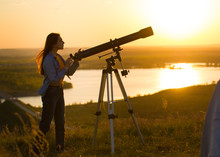 Silhouette Of Young Woman Looking View Through The Telescope At Summer Sunset