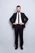 © deagreez - Full size fullbody portrait of cheerful attractive business person wearing black suit with tie looking at camera, holding hands on waist, isolated on grey background