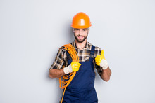 Portrait Of Handsome Joyful Electrician In Hardhat, Overall, Shirt With Bristle, Holding Rolled Wires On Shoulder, Showing Thumb Up Recommend Approve Sign Over Grey Background