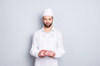 Portrait with copy space, empty place of handsome attractive butcher demonstrate fresh meat in his arms, looking at camera, isolated on grey background, advertisement concept