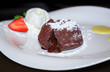 Теплый шоколадный фондант с шариком мороженого и клубникой на белой тарелке.