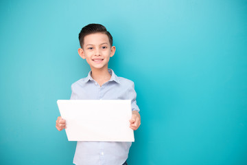 Young boy isolated in blue. Handsome early teenage boy portrait. Holding a white sign board, happy smile.