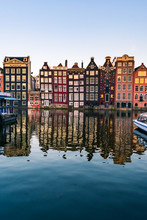 View Of Colorful Facades Of Typical Amsterdam Houses Reflecting In The Amstel River Canal In Amsterdam During Sunset