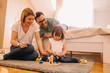 © Nebojsa - Young parents and their daughter are playing with a wooden game on floor in bedroom