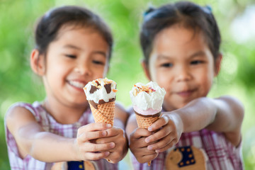 two asian little girls holding delicious ice cream waffle cone together in hand with fun and happine
