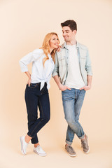 Wall Mural - Full length image of positive caucasian couple man and woman in denim clothing smiling and looking at each other, isolated over beige background