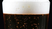 A mug of beer on a black background rotates. beer small bubbles slowly rise.