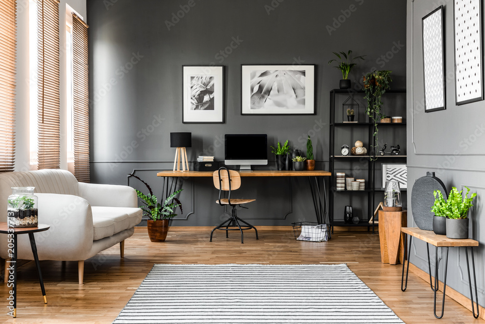 Real photo of open space apartment interior with beige sofa next to the window and desktop computer o a wooden desk - obrazy, fototapety, plakaty 